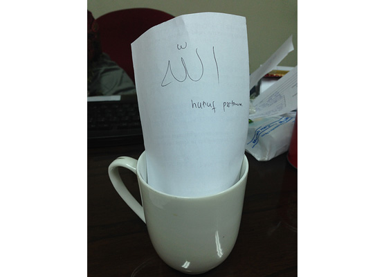 水を入れたマグカップにアラビア文字とインドネシア語を描いた紙をつけている写真
