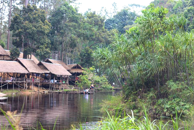 ジャングルに囲まれた川沿いに立ち並ぶ小屋の写真