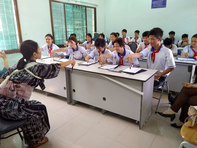 日本語パートナーズ ベトナム バリアブンタウ 大久保さんが宙に線を描いて筆を操る動きしています。動きを忠実に真似している生徒たちの写真