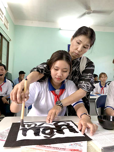 日本語パートナーズ ベトナム バリアブンタウ 生徒の手を取り、半紙いっぱいに思いっきり書いていいと筆の運びで教えている写真