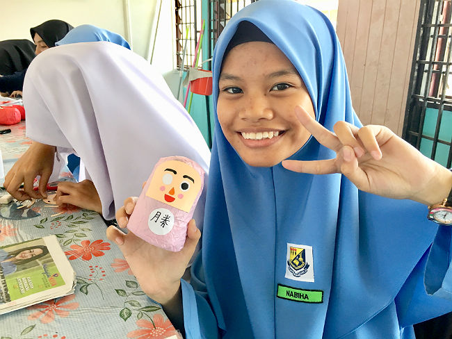 日本語パートナーズ マレーシア ジョホール州 おなかに「勝」の文字を入れただるまを手に持った女生徒の写真