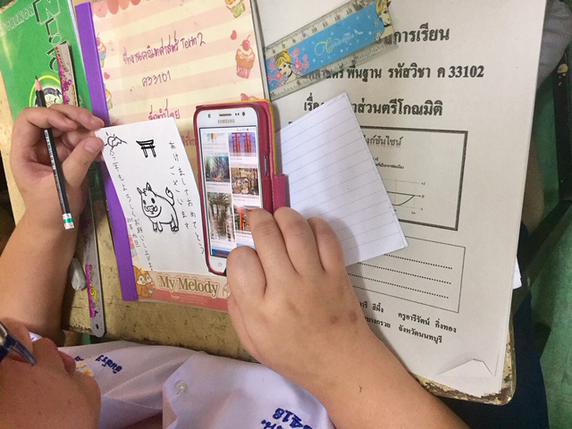 スマートフォンで調べながら年賀状のイラストを描く生徒の写真