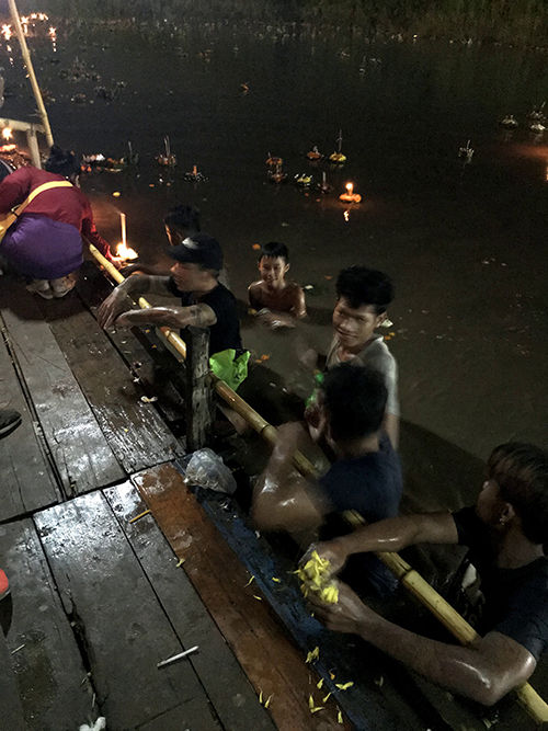 ボートに乗って岸で待機する男性たちと背後に灯篭が流れている写真