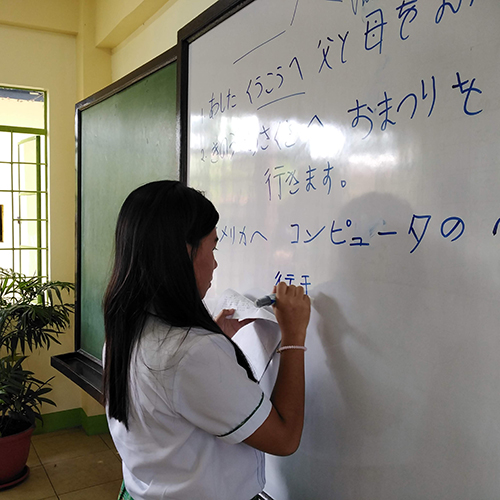 ホワイトボードに日本語文章を書く女子生徒の写真
