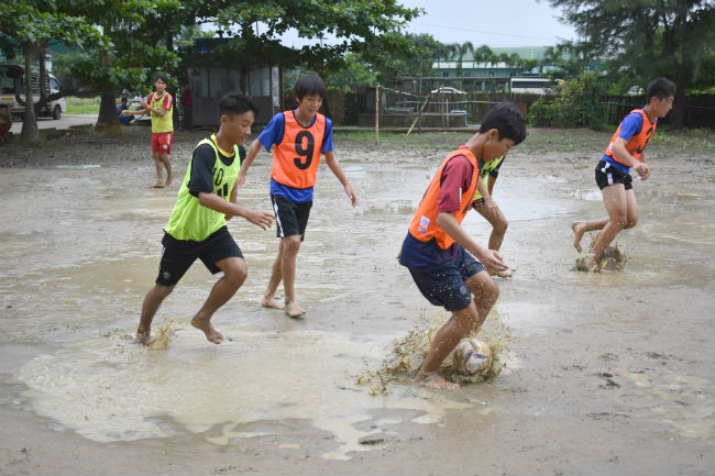 水たまりだらけのグラウンドでサッカーをする生徒たちの写真