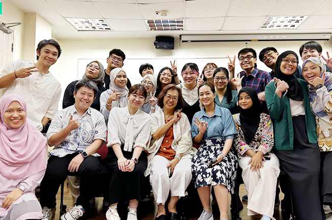 About 20 participants gathered in the classroom for a group photo, giving thumbs up and peace signs.