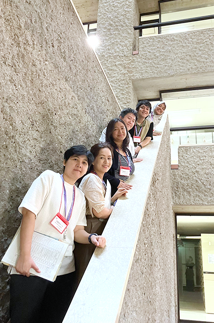 Six participants lined up on the stairs in a space with an open atrium spanning several floors and walls that resembled stone.