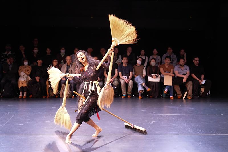 There is a woman holding two brooms in each hand.
