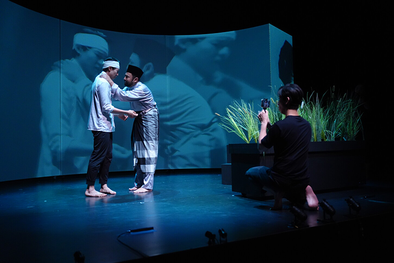 On stage, a man is lamenting with his hand on another man's shoulder.