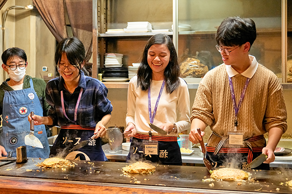 広島でのウェルカムレセプションとして、実店舗で本格的なお好み焼き作り体験をしている3名と、後ろに1名店員が写っている。