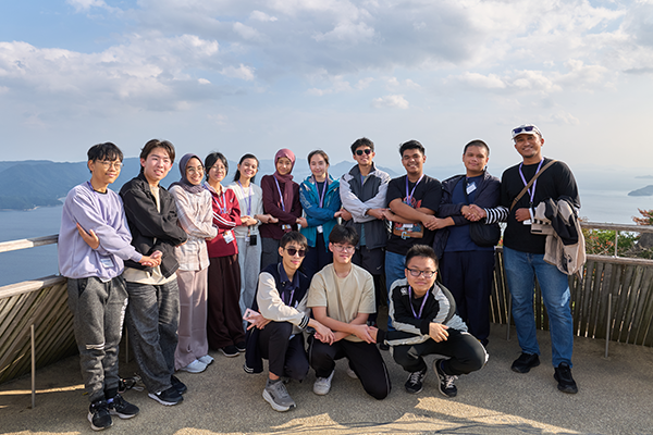 宮島の弥山山頂にて、14名が隣の人と握手をしながら写っている集合写真。