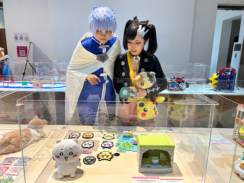 アニメやゲームのコスプレをしている2人が、展示されているちいかわグッズを見ている。