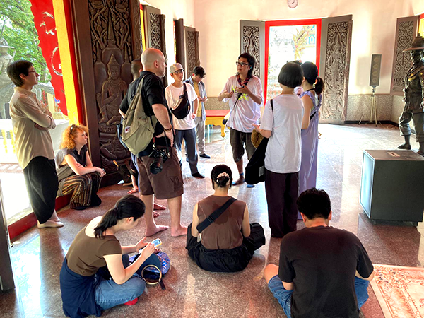 タイの寺院のような場所で、ガイドが参加者に向けてレクチャーを行っている。